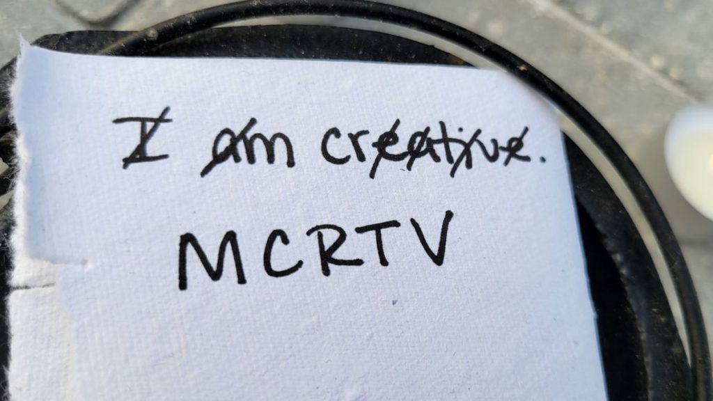 A white paper with the phrase, "I am creative" written on it. The vowels and consonants are crossed out and the remaining letters are written: MCRTV