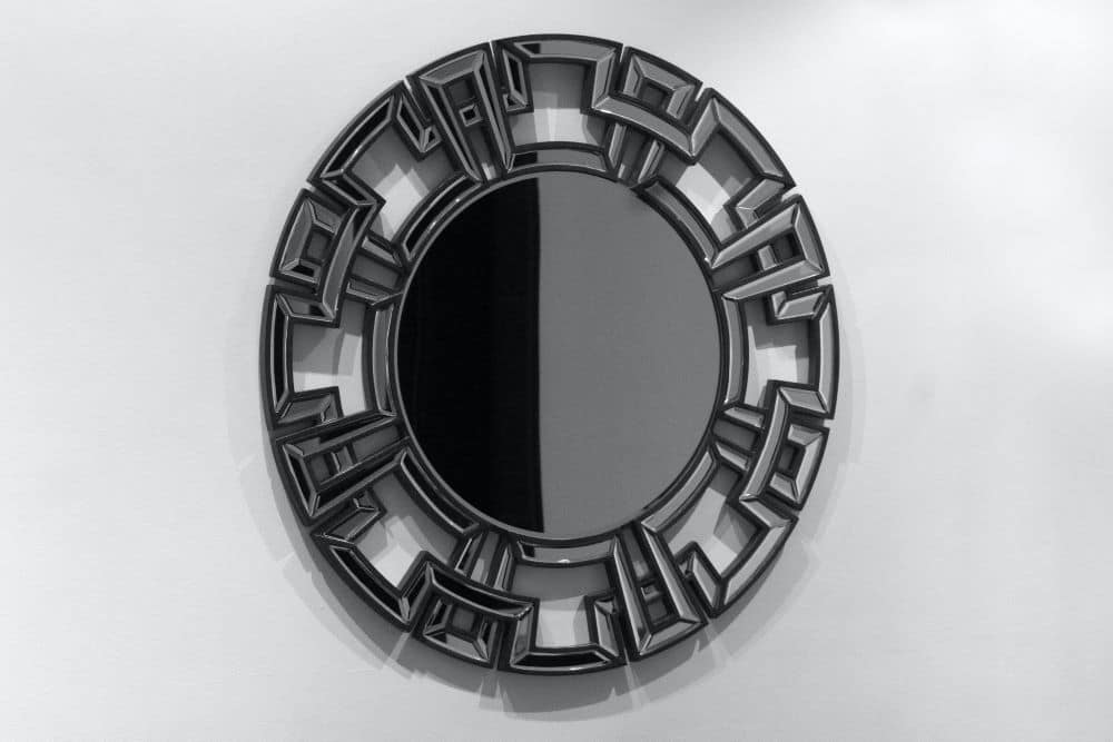 A black mirror hangs on a white wall.